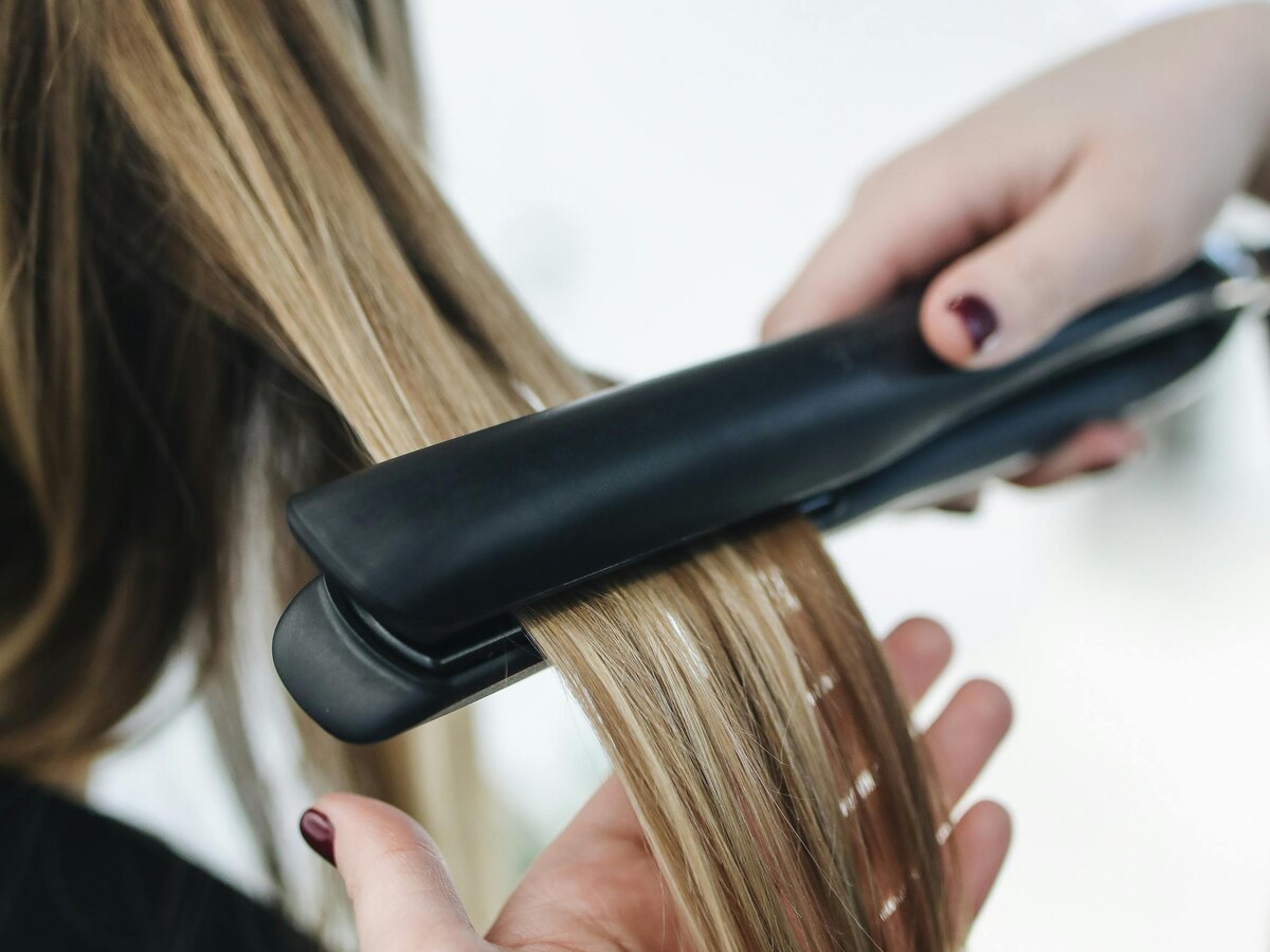 Close-up of blonde highlighted curls being styled with a flat iron