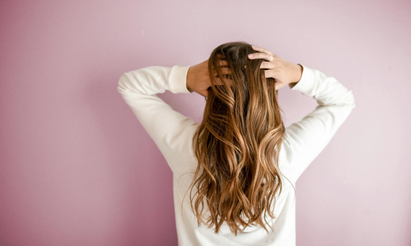 Long wavy hair photographed from behind against a soft pink wall